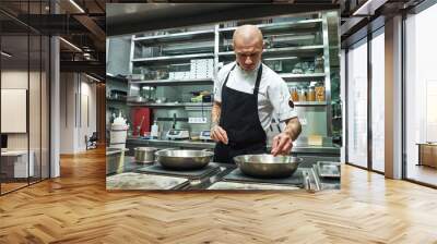 Confidence in everything. Serious male chef with several tattoos on his arms frying ingredients for his dish in a restaurant kitchen Wall mural