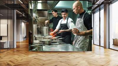 Dangerous work. Profesional chef teaching his two young trainees how how to flambe food safely. Cooking techniques Wall mural