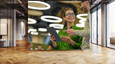 Discussing project. Young positive asian woman showing something on digital tablet to her male colleague while standing together in the coworking space or office Wall mural