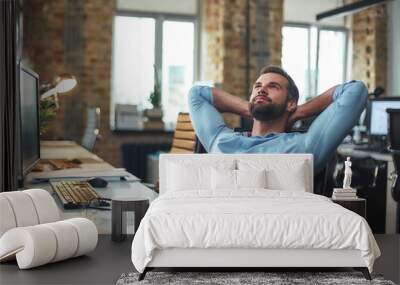 Enjoying break. Satisfied young bearded businessman leaning back with hands behind head and relaxing while sitting in the modern office Wall mural