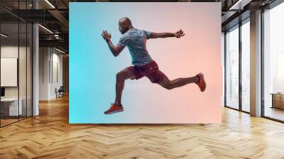 Full length of young african man in sports clothing jumping against colorful background Wall mural