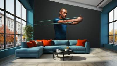 Get stronger every day. Sportsman working out with resistance band over dark background Wall mural