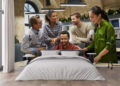 Group of young happy business people looking at laptop screen, communocating and discussing work while standing together in the modern office Wall mural