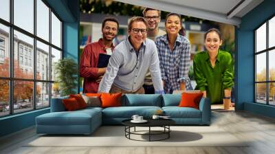 Group of young successful multi ethnic business team looking at camera and smiling while having a meeting in the modern office and coworking space Wall mural