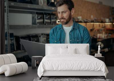 Handsome repairman in own workshop working on laptop Wall mural