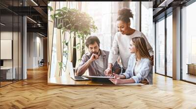 Happy multiracial millennial colleagues discussing company financial statistics at briefing in office, employees brainstorming analyzing growing sales, developing success strategies, reading reports Wall mural