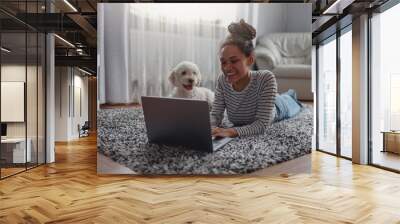 Happy positive female searching internet on laptop computer at cozy house on carpet Wall mural