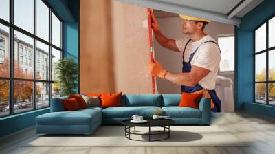 Joyful male builder measuring wall in house Wall mural