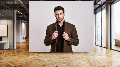 Looking just perfect. Stylish dark-haired man holding his jacket and looking at camera isolated over grey background Wall mural