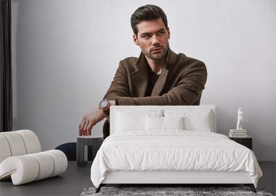 Perfect style. Stylish dark-haired man sitting on a chair and looking away isolated over white studio background Wall mural