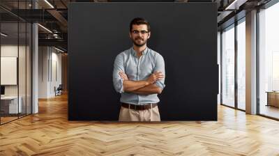 Project manager. Confident and young bearded man looking at camera with smile and keeping arms crossed while standing against dark background Wall mural