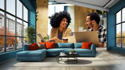 Sharing fresh ideas. Two young happy multiracial business people sitting at desk and communicating while working together in coworking space Wall mural