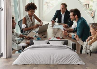 Sharing new ideas. Group of young business people discussing something and smiling while sitting at the office table Wall mural