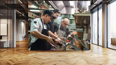 Teamwork. Restaurant chef and his two assistants in aprons cooking a new dish in a modern kitchen. Wall mural