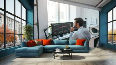 Trading on world markets. Young stock market broker analyzing data and graphs on multiple computer screens while sitting in modern office Wall mural