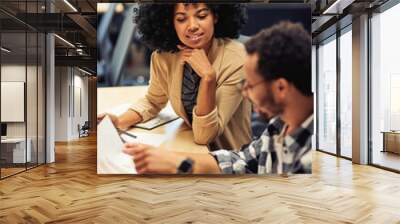 Two young diverse coworkers analyzing sales report while working together in the office Wall mural