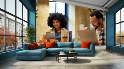 Two young happy multiracial business people sitting at the desk, using modern technologies while working together in coworking space Wall mural