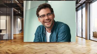 We have great results Young handsome man in eyeglasses discussing something with colleagues and smiling while sitting in the modern office Wall mural