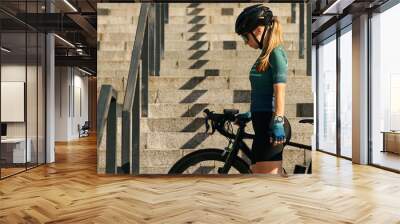 Website header of Full length shot of professional female cyclist in cycling garment and protective gear standing on the steps with her bike after having a training, riding in city center Wall mural