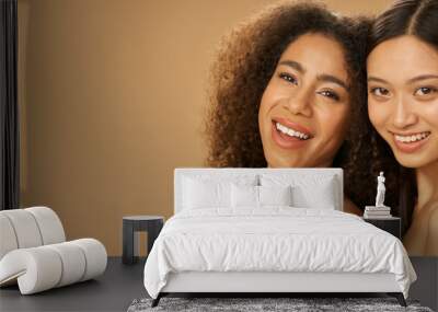 Website header of Portrait of two joyful attractive mixed race young women with perfect smile posing for camera isolated over beige background Wall mural