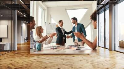 Welcome to our team Two cheerful colleagues shaking hands and smiling while having a meeting in the modern office Wall mural