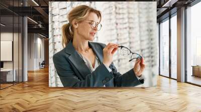 Woman in jacket chooses between two glasses in an optician's shop  Wall mural