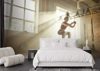 Working out. Side view of beautiful athletic woman in sportswear training legs at gym. Wall mural