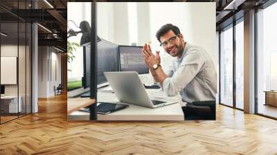 Young and successful. Happy bearded trader in formal wear and eyeglasses looking at camera and smiling while sitting in his modern office. Wall mural