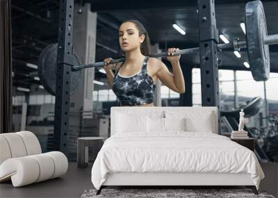 Young brunette woman exercises in gym pulling weights with ropes looking forward motivated close-up Wall mural