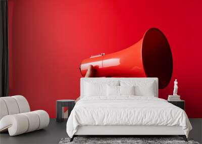 A hand holds a red megaphone on a red background Wall mural