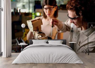 Two young engineers fixing a mechanical robot in the workshop, wearing industrial glasses Wall mural