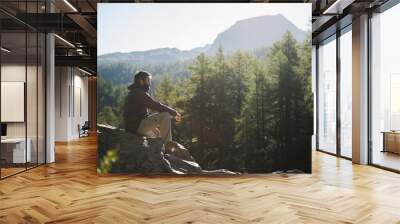 young adult active man sitting on top rock looking at panorama in sunny spring summer morning on mou Wall mural