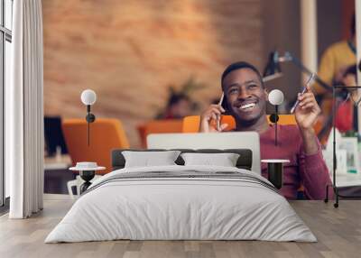 African American businessman on the phone sitting at the computer in his startup office Wall mural