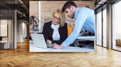 Colleagues chatting, sitting together at office table, smiling Wall mural