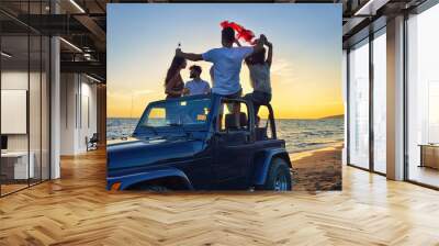 Five young people having fun in convertible car at the beach at sunset. Wall mural