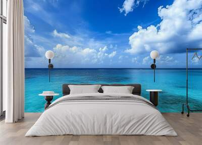 A calm blue ocean with white clouds in a clear sky. Wall mural