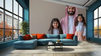 A Middle Eastern father with his two daughters, smiling and looking at the camera, in traditional clothing against a neutral background. Wall mural