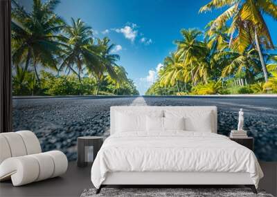 A  paved road stretches towards the horizon in a tropical paradise, bordered by lush palm trees and a bright blue sky. Wall mural