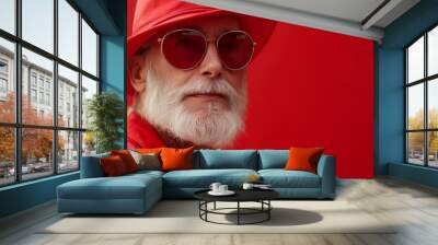 Portrait of a stylish senior man wearing a red hat and sunglasses against a red background. Wall mural