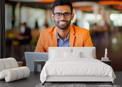 Happy Indian man in orange attire working on laptop indoors Wall mural