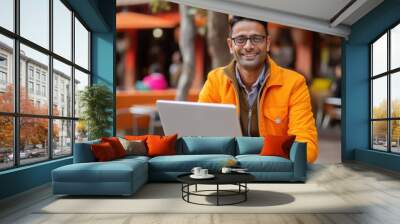 Happy Indian man in orange attire works on laptop outdoors Wall mural