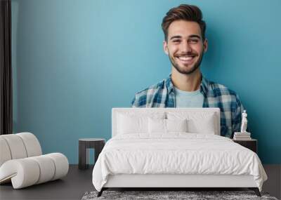 Portrait of a handsome man with a friendly smile, wearing a smart casual outfit, standing against a plain blue background. Wall mural