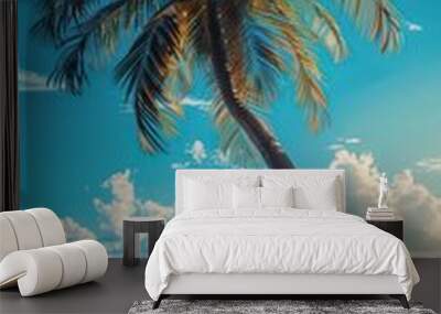 A palm tree shades two wooden chairs on the sandy beach, creating a relaxing spot with a picturesque view of the ocean and clear blue sky. Wall mural