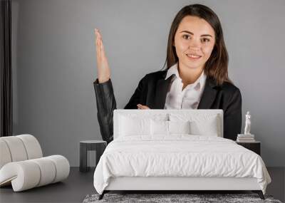 girl in black jacket on grey background pointing up Wall mural