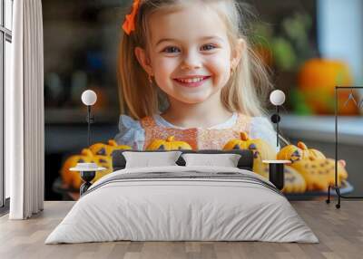 A happy little girl holds a tray of homemade halloween pumpkin shaped cookies Wall mural