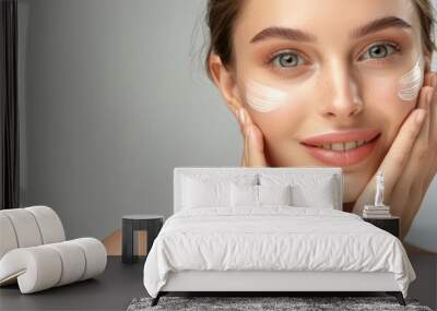 A fresh-faced young woman applies facial cream, representing beauty routines and skincare Wall mural