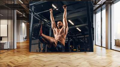 A man doing ABS workouts on pull up bar in a gym club. Wall mural