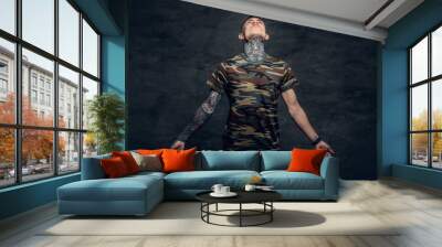 A man with tattoos on his neck, face and arms, dressed in a camouflage t shirt. Wall mural