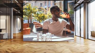 American student is drinking fruit juice at cafe on hot sunny day. Wall mural