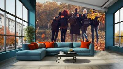 Back view of young friends hugging together and looking at the lake in beautiful autumn forest. Wall mural